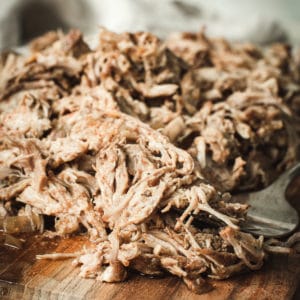 Pulled pork on cutting board with silver fork.