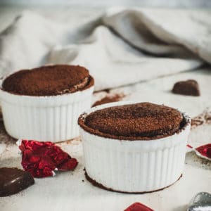 Two chocolate soufflés in white ramekin bowls.