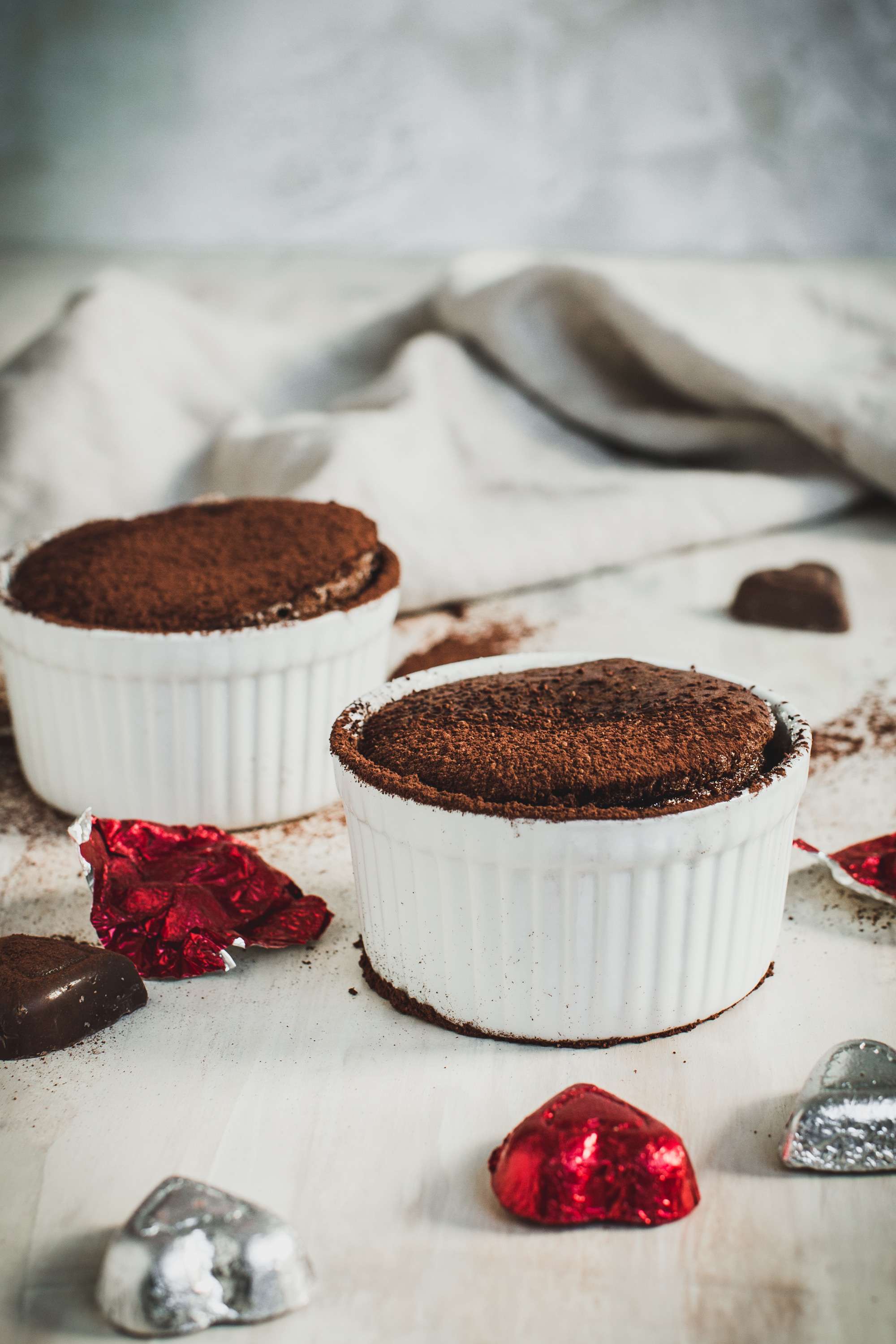 Two chocolate soufflés in white ramekin bowls.