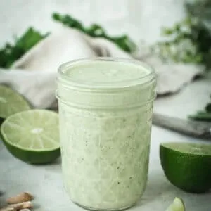 Lime crema in a glass jar surrounded by cashews and lime halves.