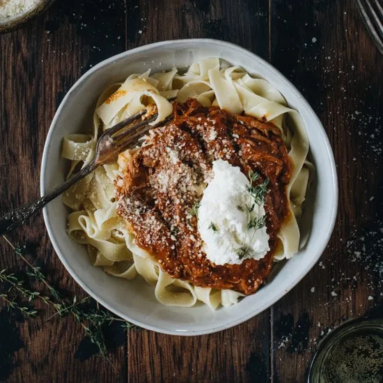 Pasta topped with a red sauce and ricotta cheese in a white bowl.