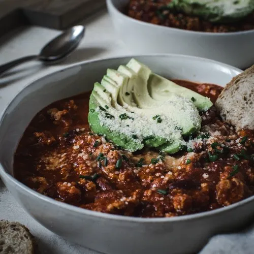 Turkey chili topped with avocado sliced in a white bowl.