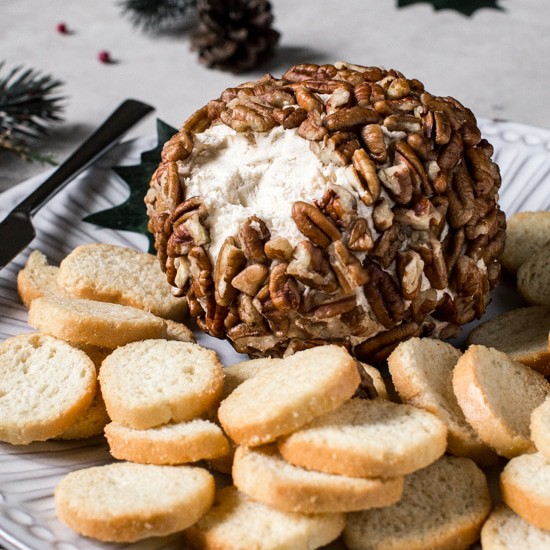 Cheese ball with scoop cut out on a plate with mini toasts.