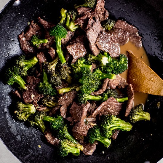 Beef and broccoli stir fry in a wok with a wooden spatula.