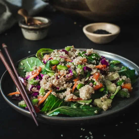 Asian sesame quinoa salad on black plate with brown chopsticks.