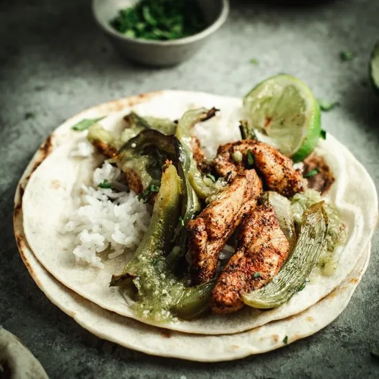 Tomatillo and chicken fajita on tortilla shells with lime in background.