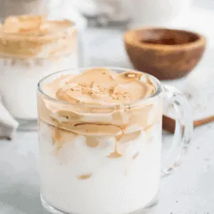 Whipped coffee in a clear glass mug.