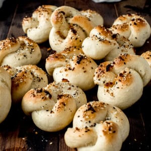 garlic knots topped with everything seasoning and piled on wooden board