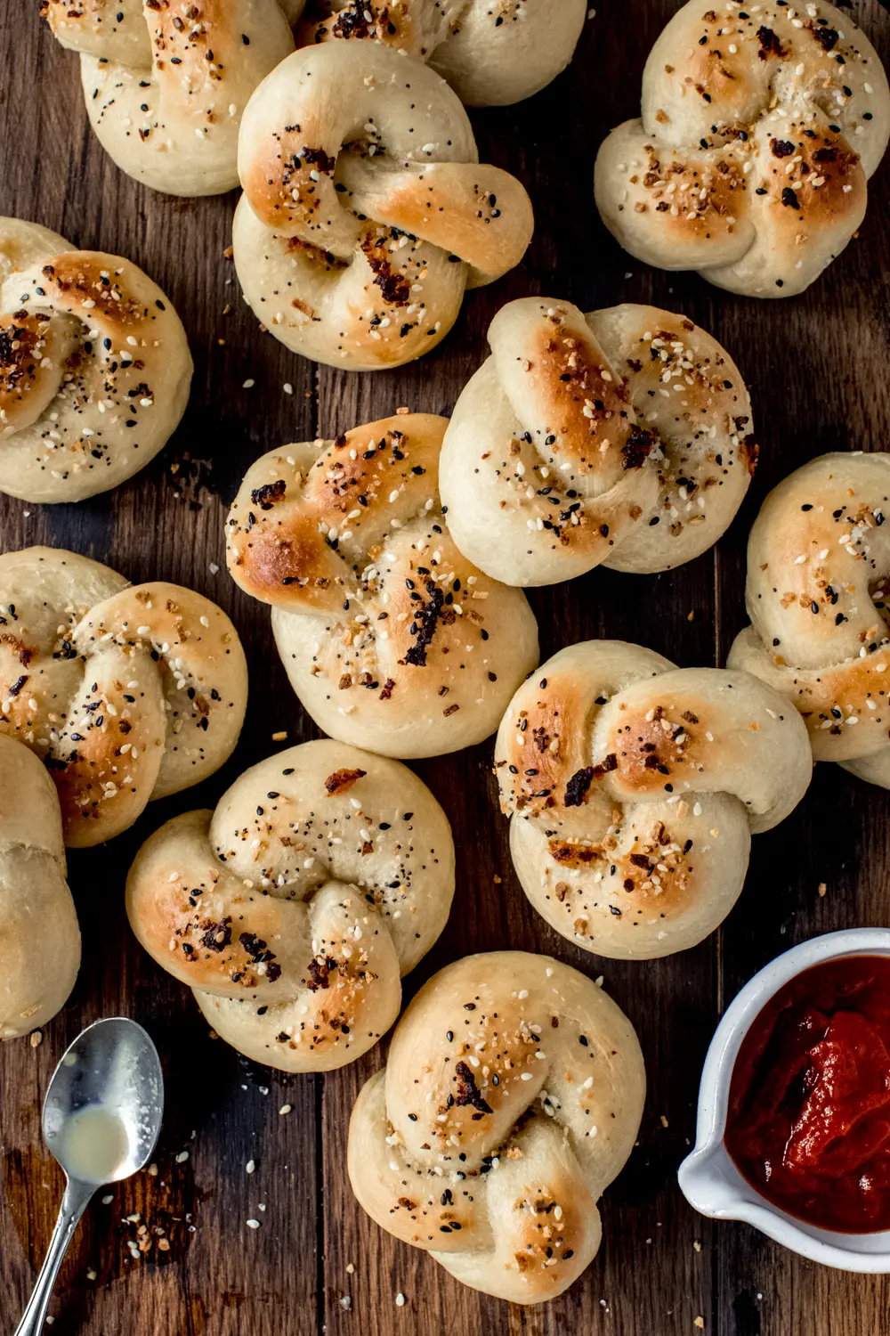 soft garlic knots topped with everything seasoning on wooden background with dipping sauce