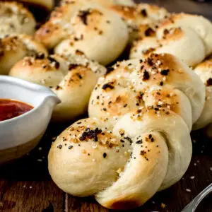 garlic knots on wooden board with buttery silver spoon and tomato sauce