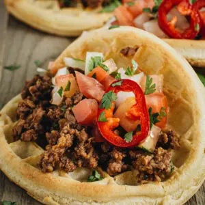 Close up of waffle taco topped with chili pepper and pico de gallo.