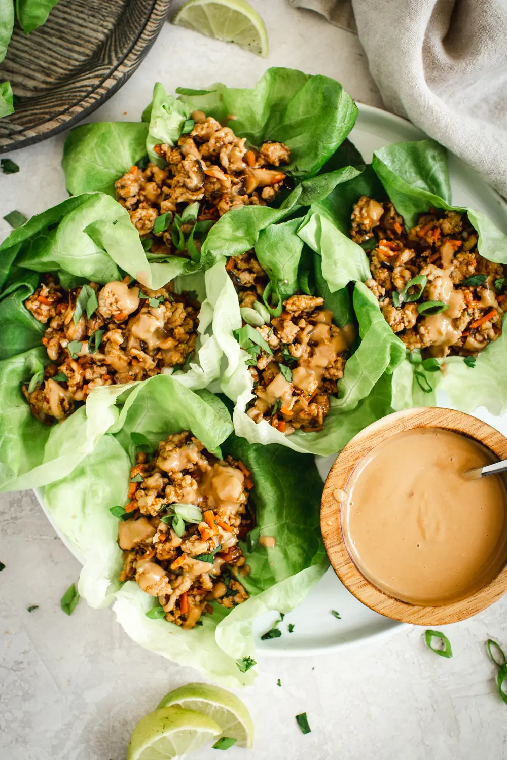 Easy lettuce wraps on round white plate with peanut drizzle sauce on the side.