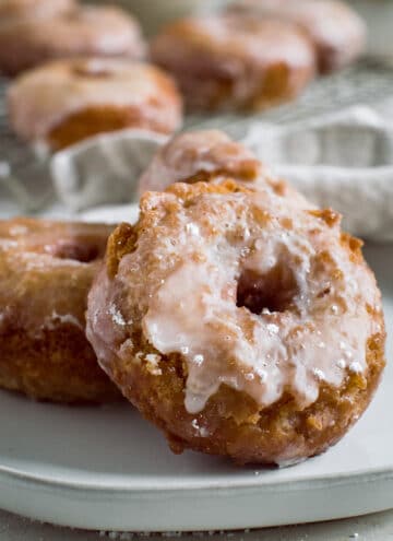 Sour cream cake donut covered in a vanilla glaze leaning against another donut.