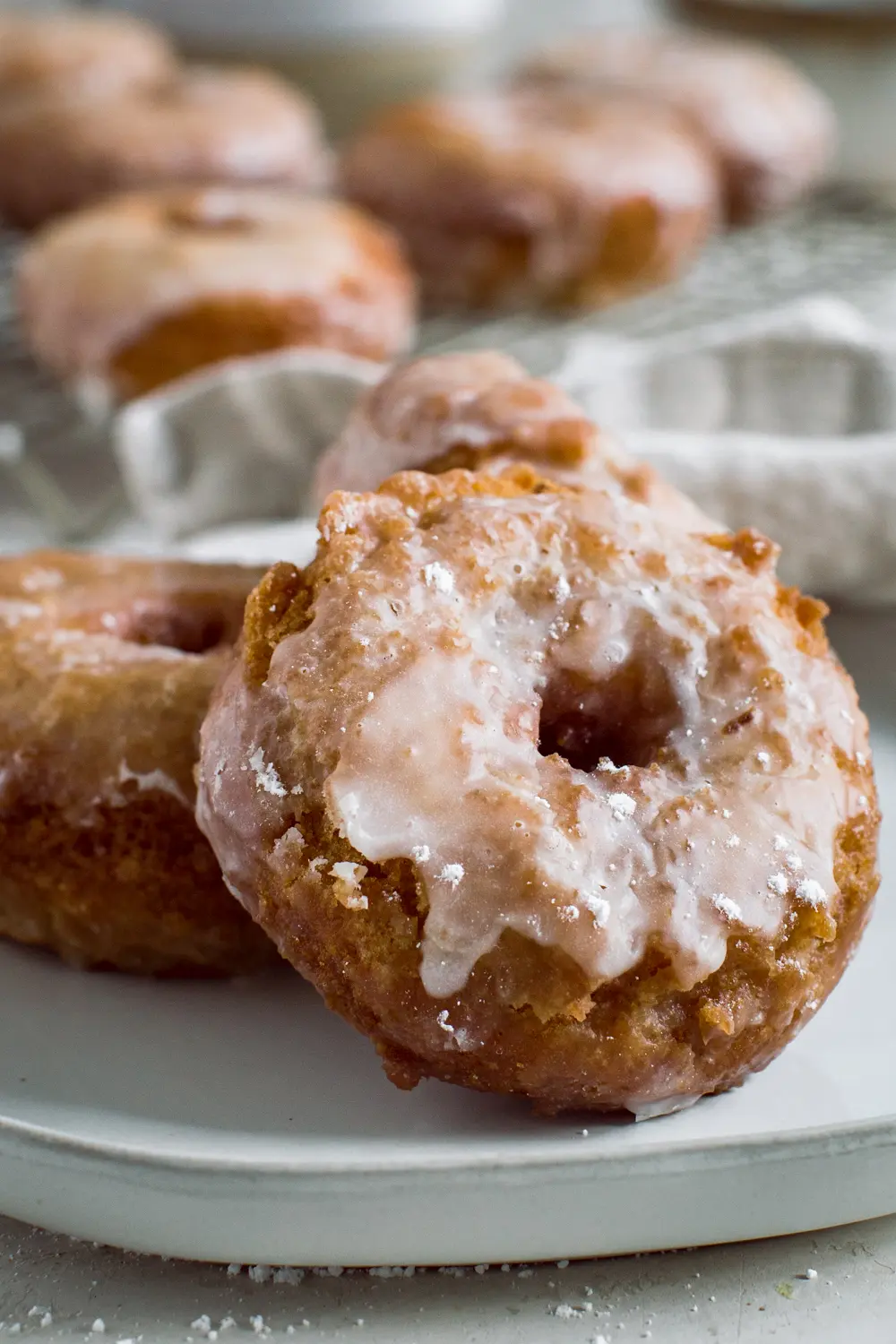 Sour cream cake donut covered in a vanilla glaze leaning against another donut.