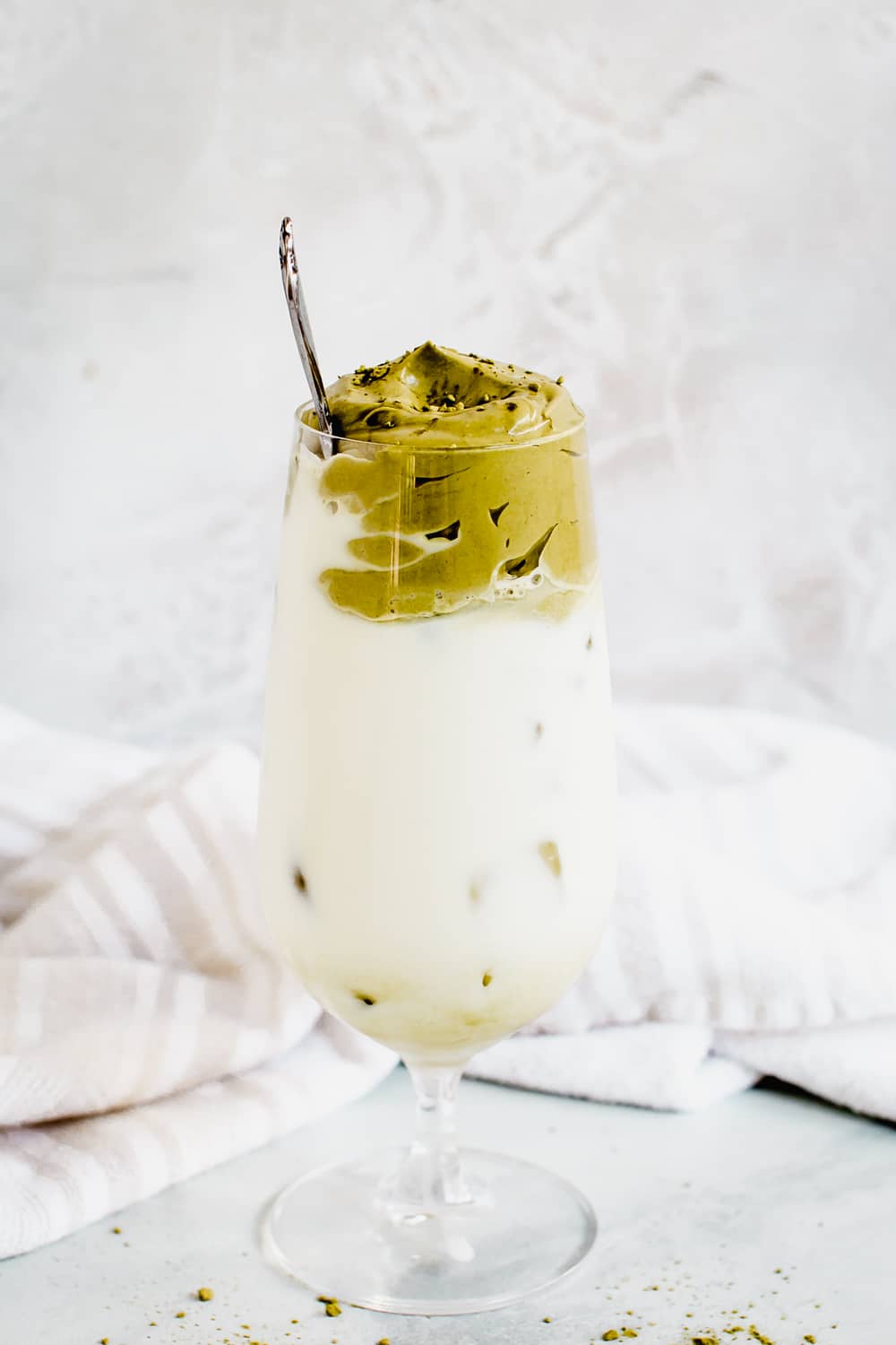 dalgona matcha latte in a clear tall glass with silver spoon stirrer