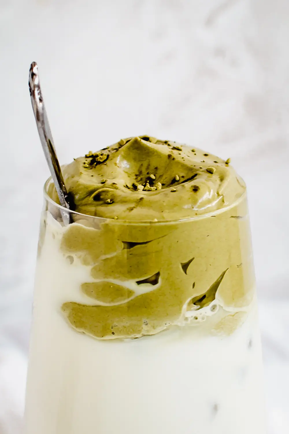 close up of whipped matcha latte in glass with matcha powder on top 