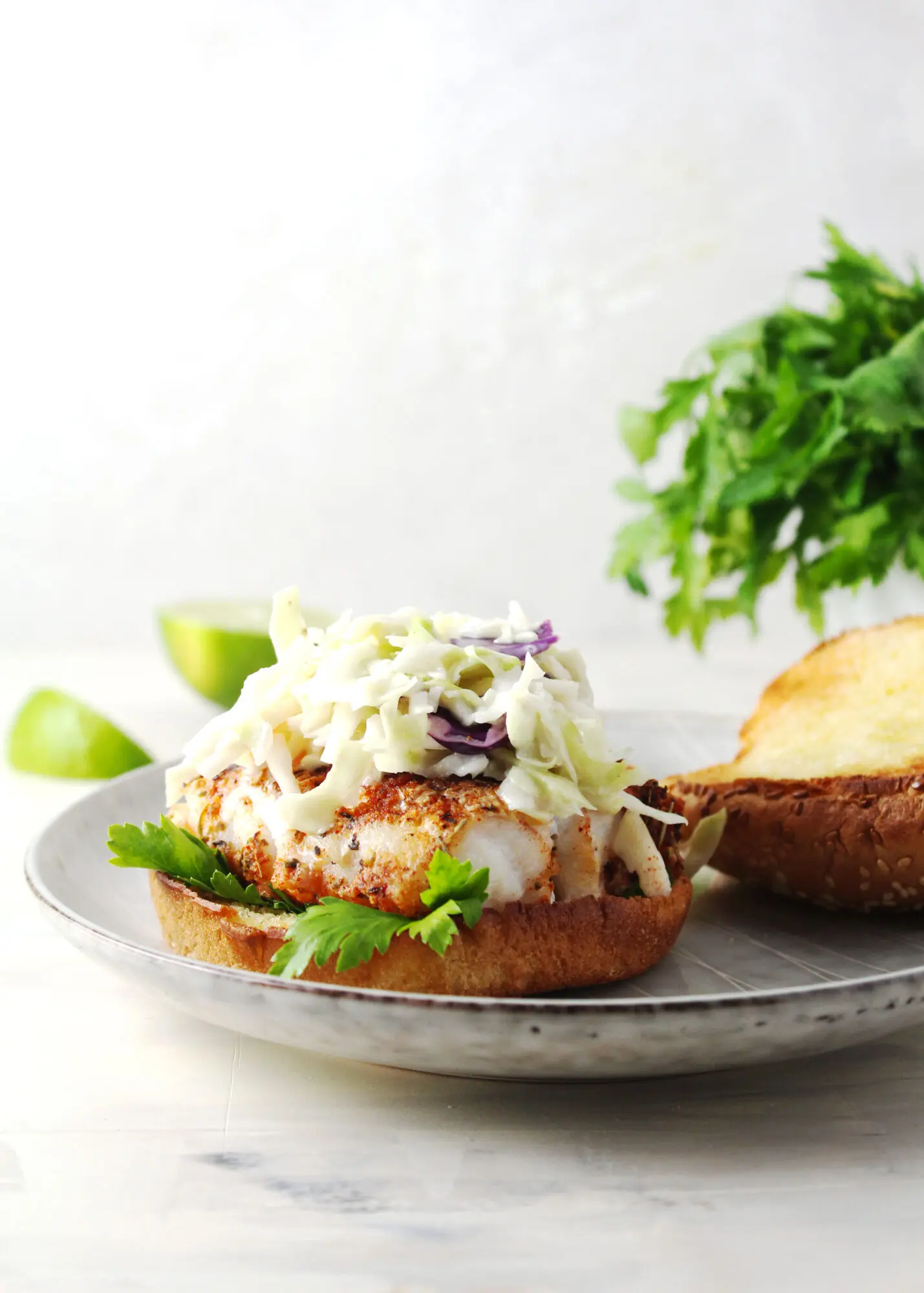fish sandwich topped with coleslaw and bun top sitting on the side