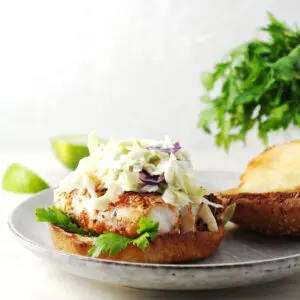 Fish sandwich topped with coleslaw and bun top sitting on the side.