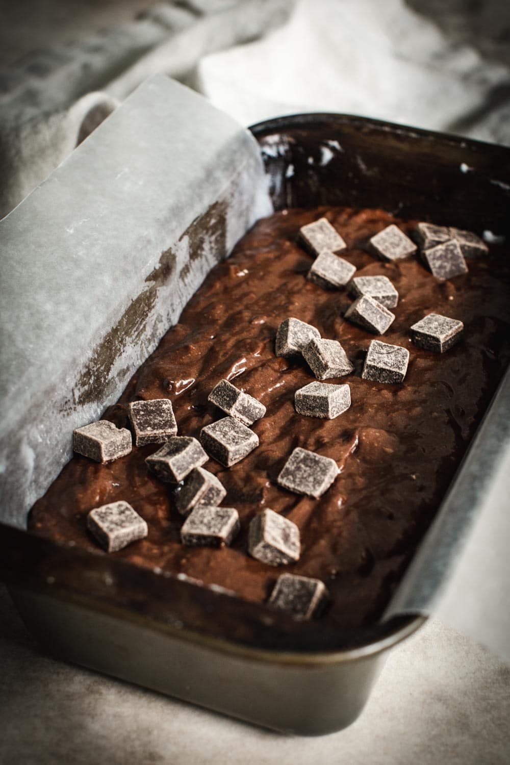 Chocolate banana bread batter topped with chocolate chunks in a loaf pan.