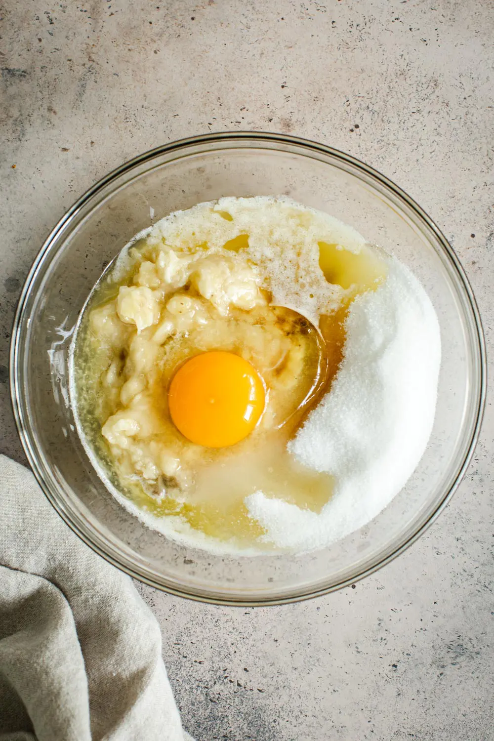 Wet ingredients for banana muffins in glass mixing bowl.