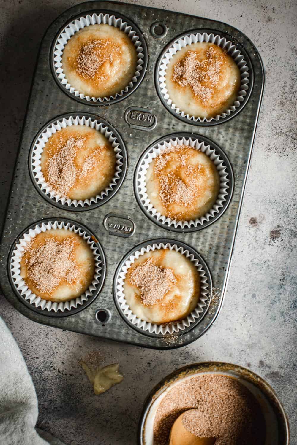 Cinnamon sugar banana muffin batter in muffin cups in a muffin tin.