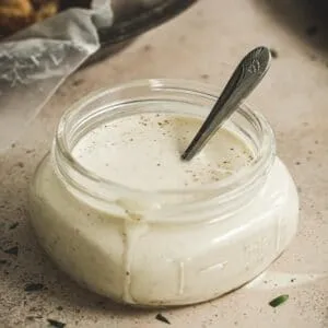 white barbecue sauce in small glass jar with silver serving spoon