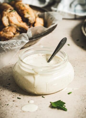 White sauce in small glass jar with silver spoon.
