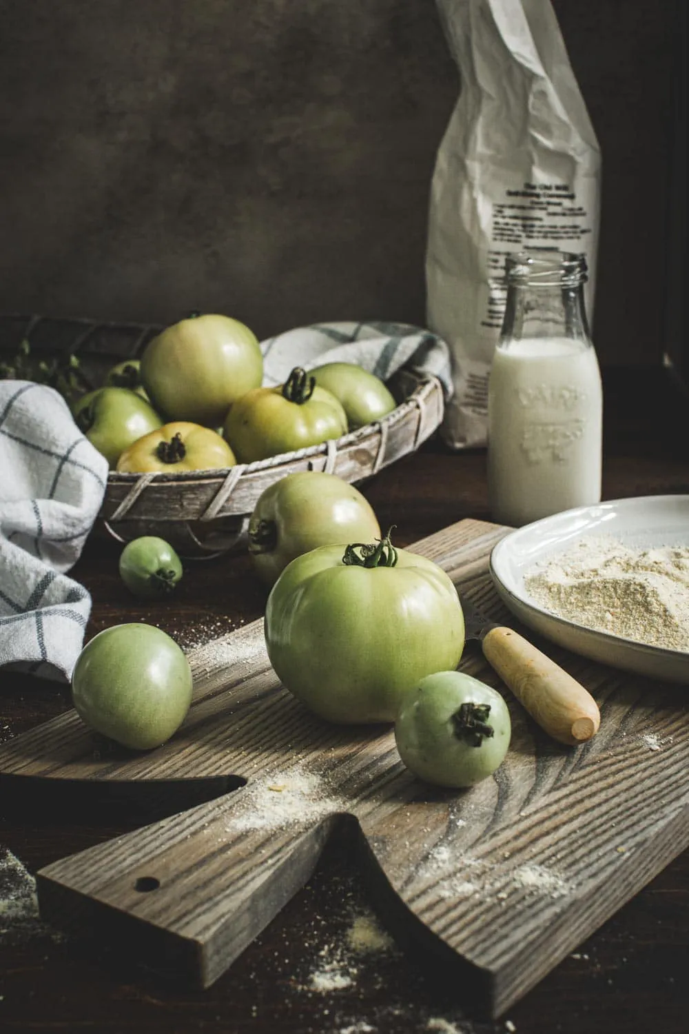 Green tomatoes on wooden cutting board next to knife.