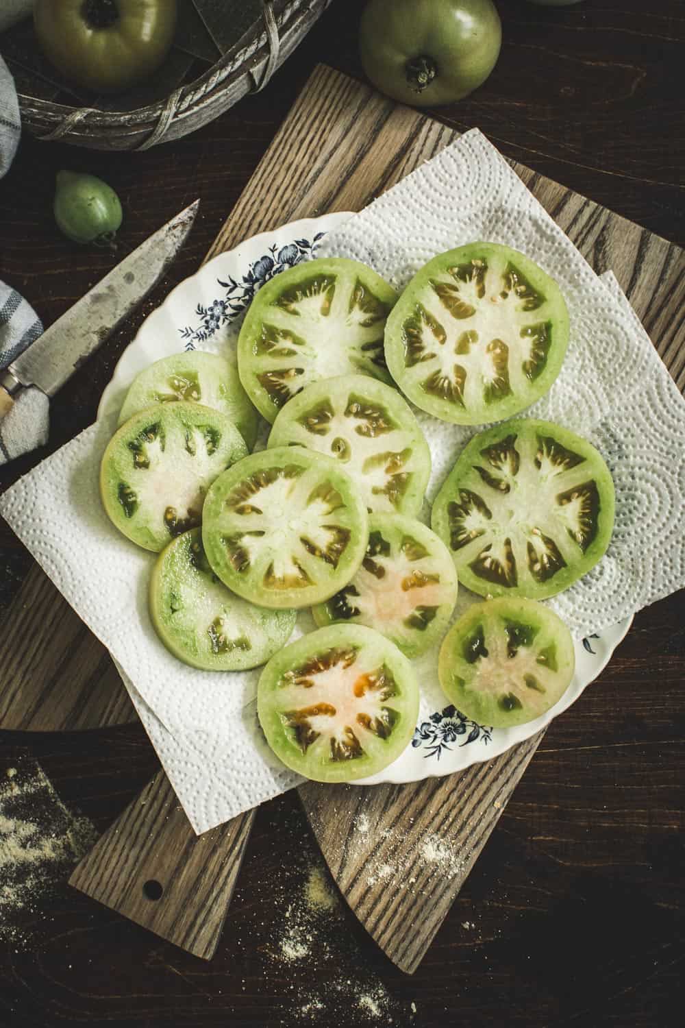 Sliced green tomatoes salted on top of paper towels on plate.