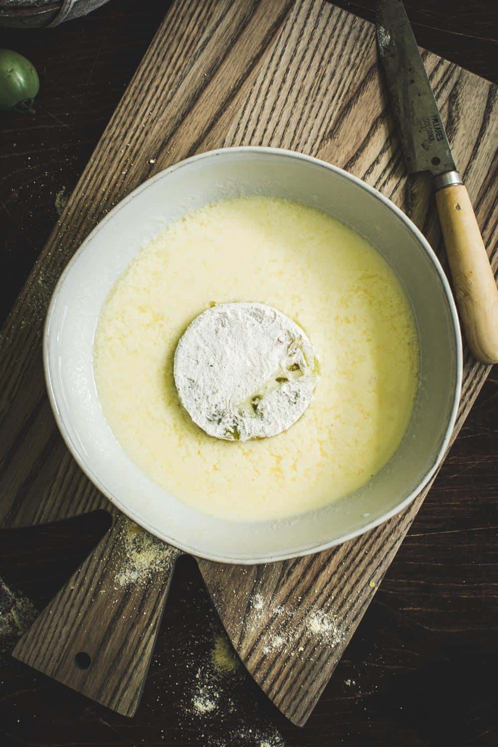 Egg wash mixture in bowl with green tomato.