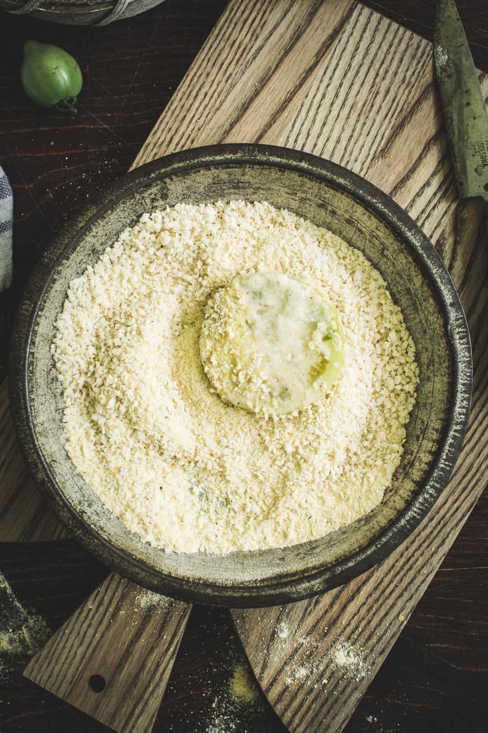Breadcrumb and cornmeal mixture in a metal tin with green tomato.