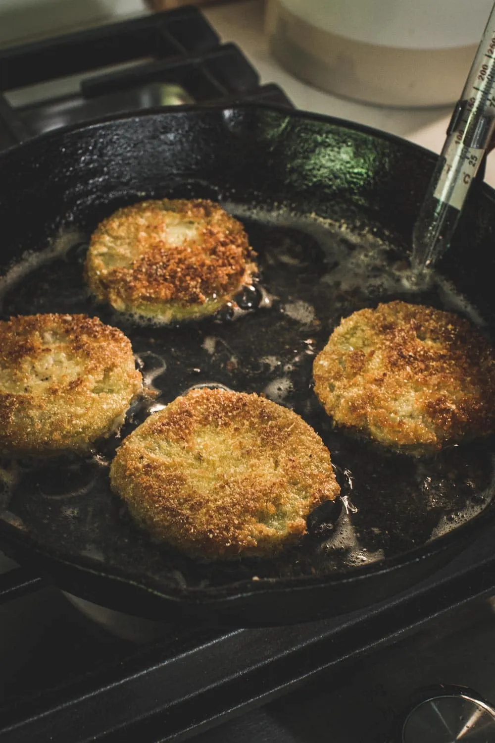 Tomatoes frying in an iron skillet with thermometer attached.