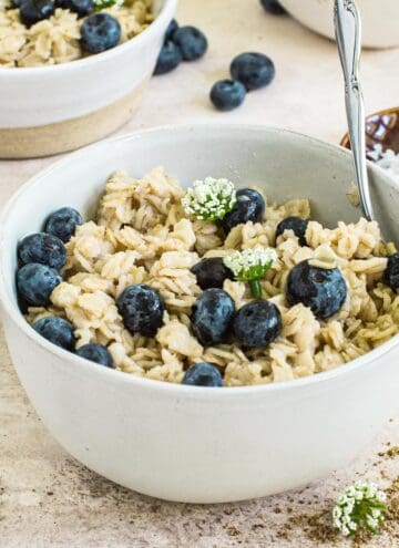 Flaxseed oatmeal covered in blueberries and syrup topped with small white flowers.