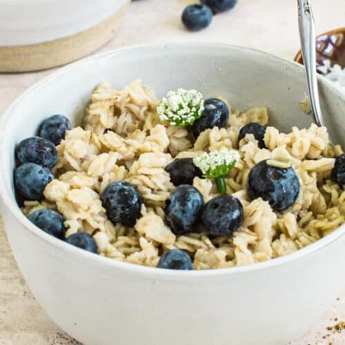 Flaxseed oatmeal covered in blueberries and syrup topped with small white flowers.
