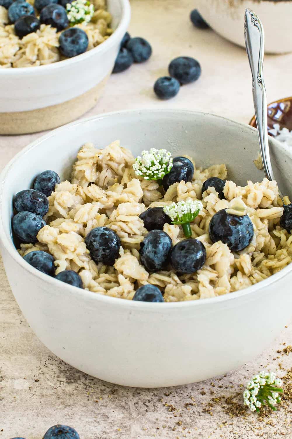 Flaxseed oatmeal covered in blueberries and syrup topped with small white flowers.