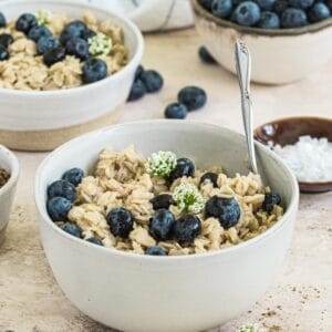 Easy stovetop oatmeal topped with blueberries in white bowl with silver spoon.