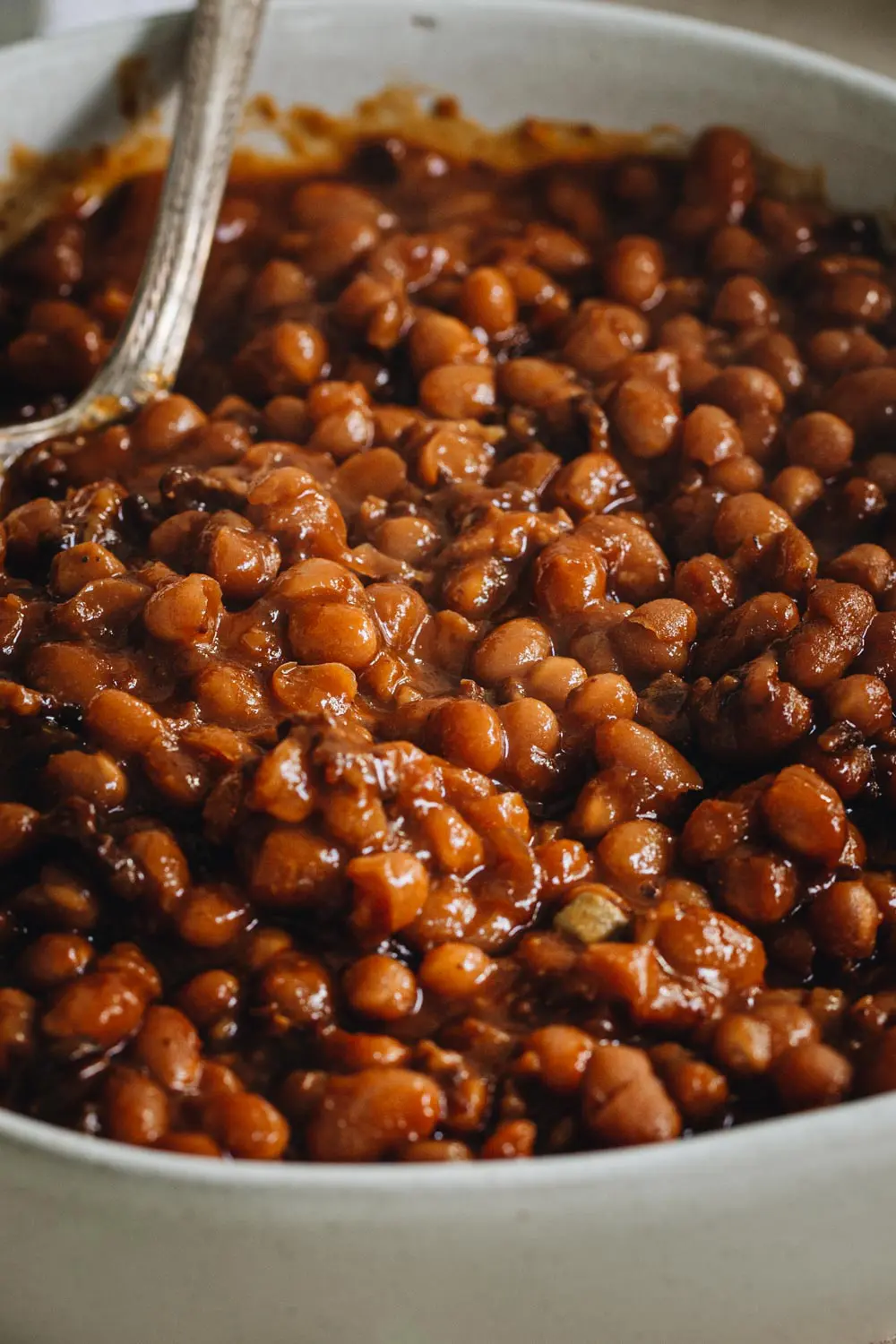 close up of smoked baked beans in a large bowl with silver serving spoon