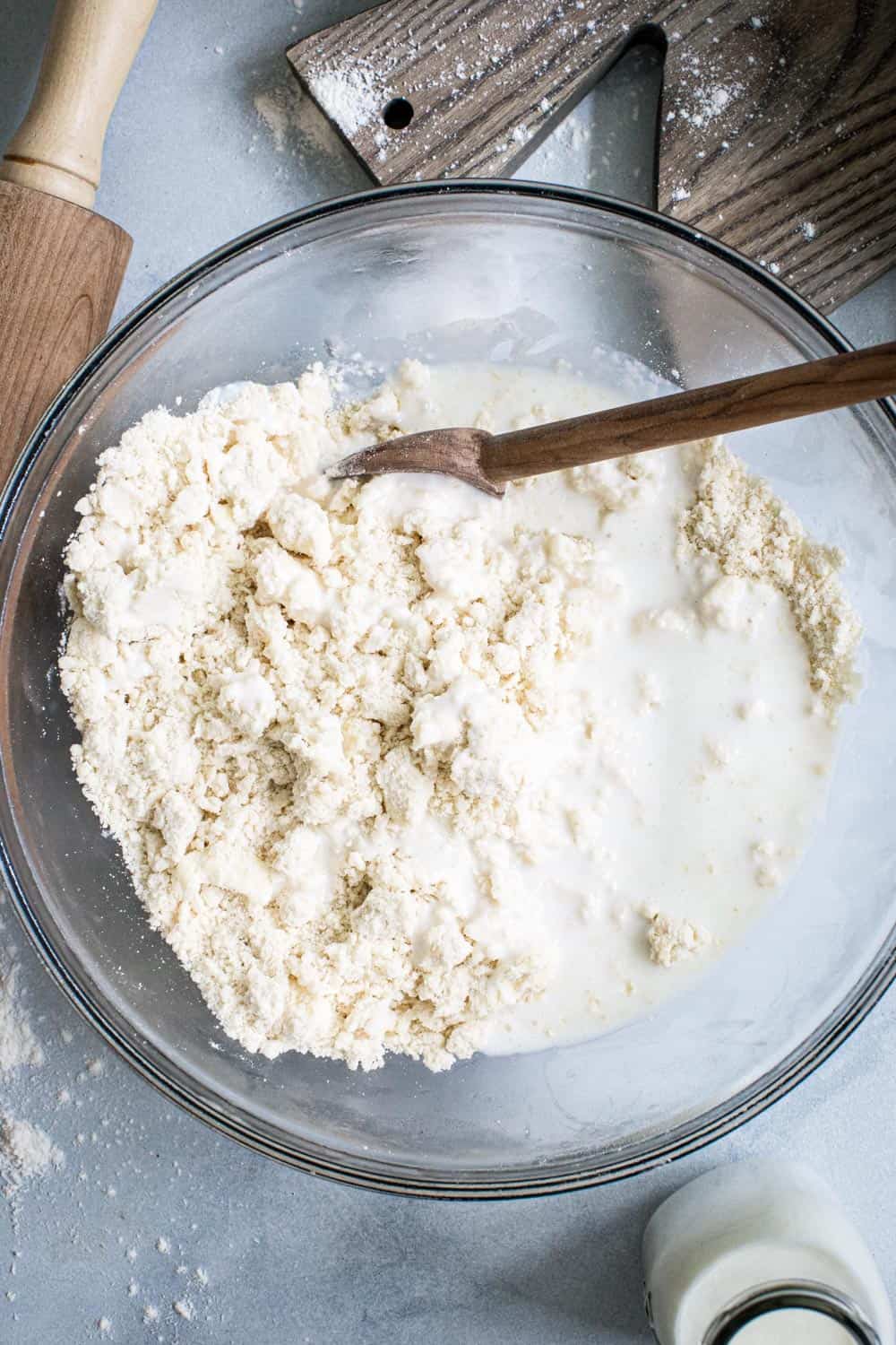 Buttermilk added to pie crust in glass bowl with wooden spoon.