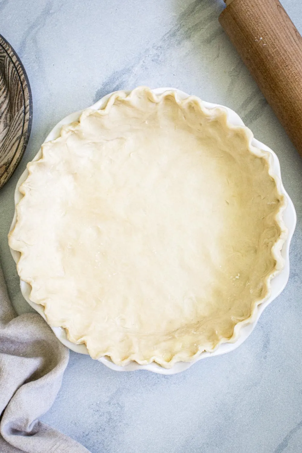 pie crust with crimped edges in white pie dish on marble surface