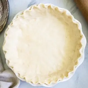 Buttermilk pie crust in a white pie dish on marble surface.