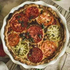 tomato pie in a white pie dish on top of a wooden cutting board