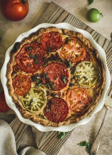 tomato pie in a white pie dish on top of a wooden cutting board