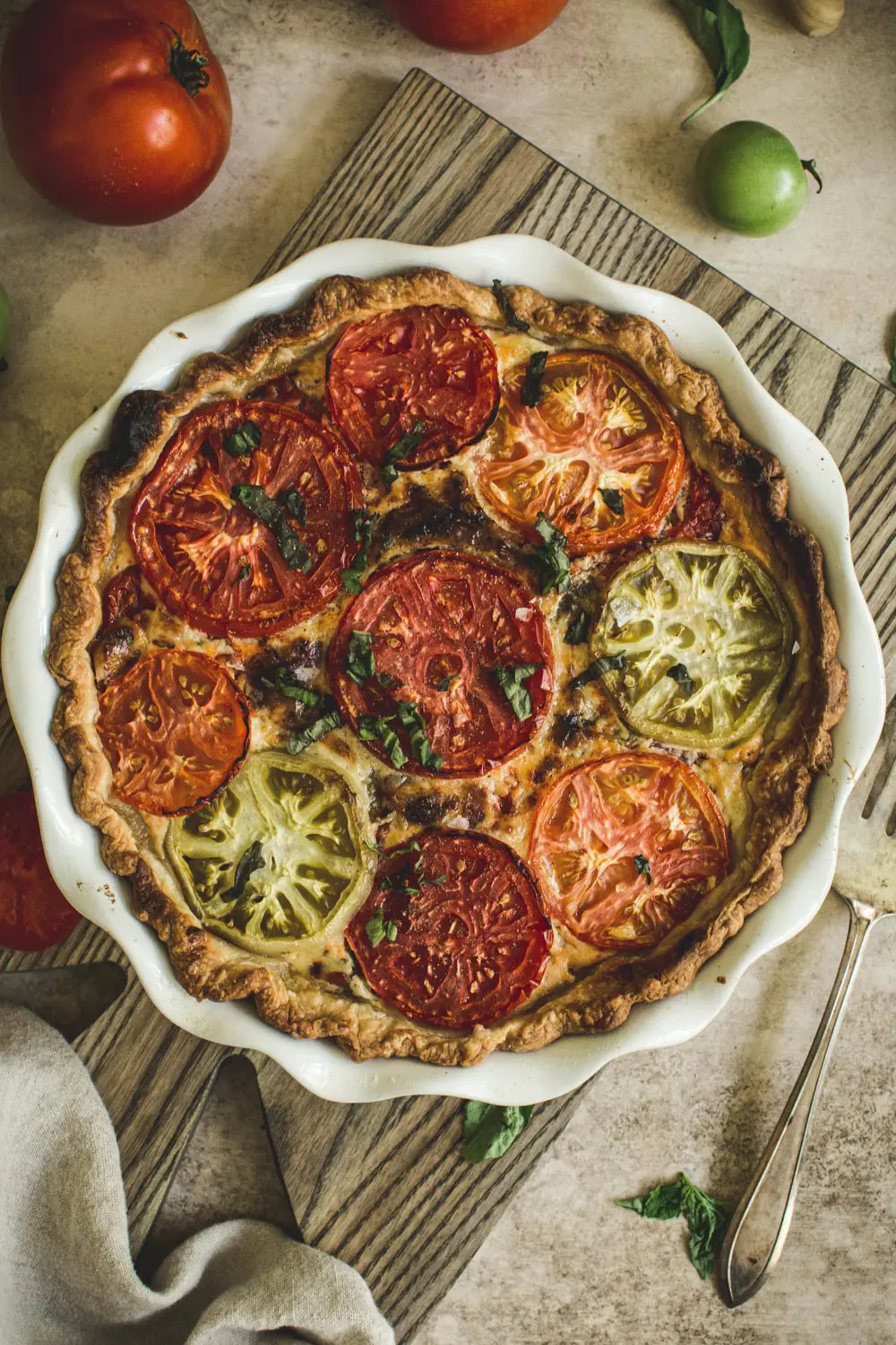 tomato pie in a white pie dish on top of a wooden cutting board