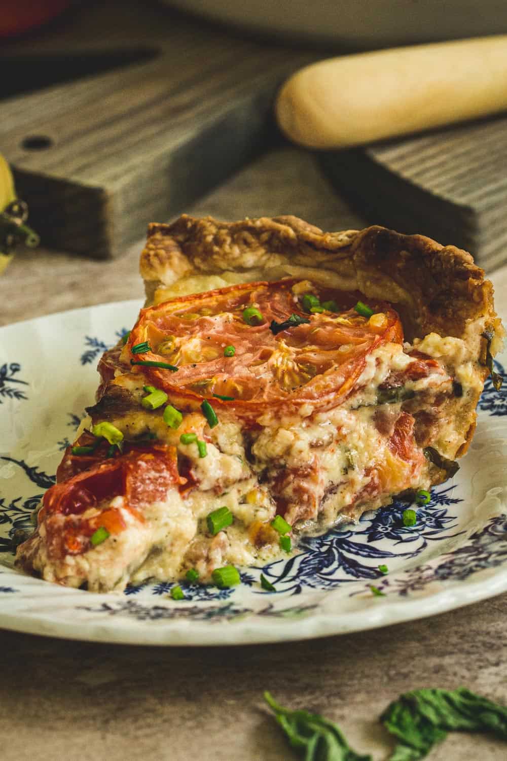 slice of tomato pie topped with chives on a blue and white plate