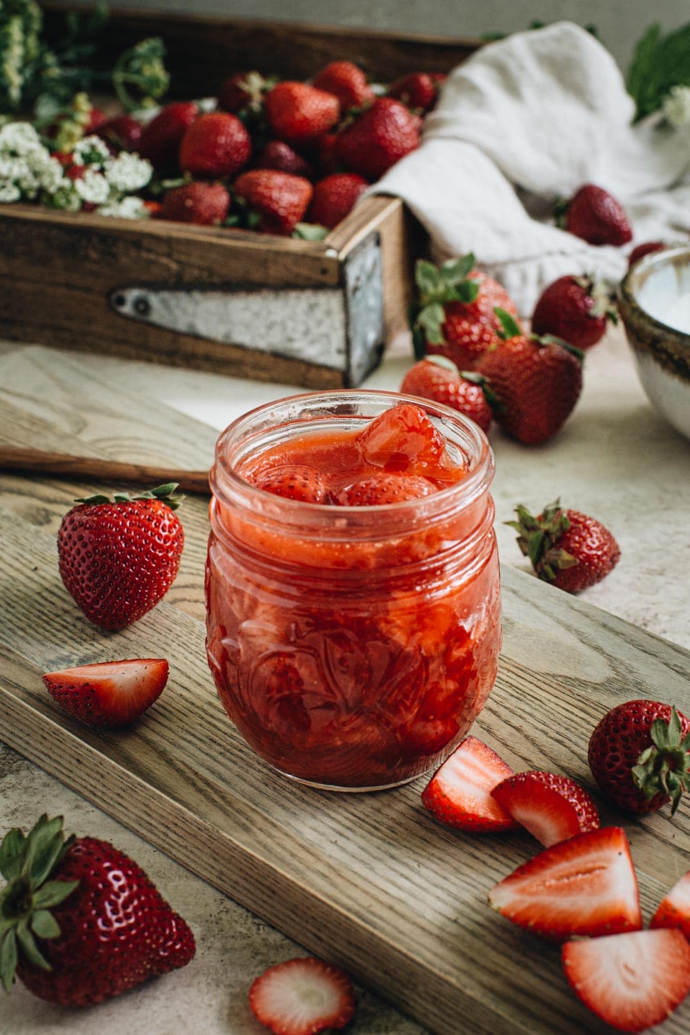 vegan strawberry sauce in a glass jar on a wooden cutting board with strawberries surrounding it
