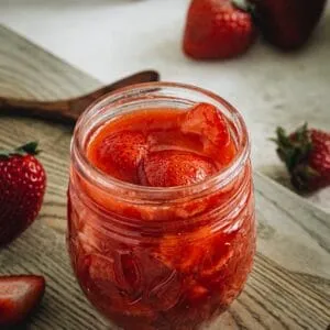 strawberry sauce in glass jar on wood cutting board