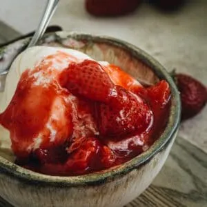 strawberry glaze on top of vanilla ice cream in a pottery bowl with silver spoon