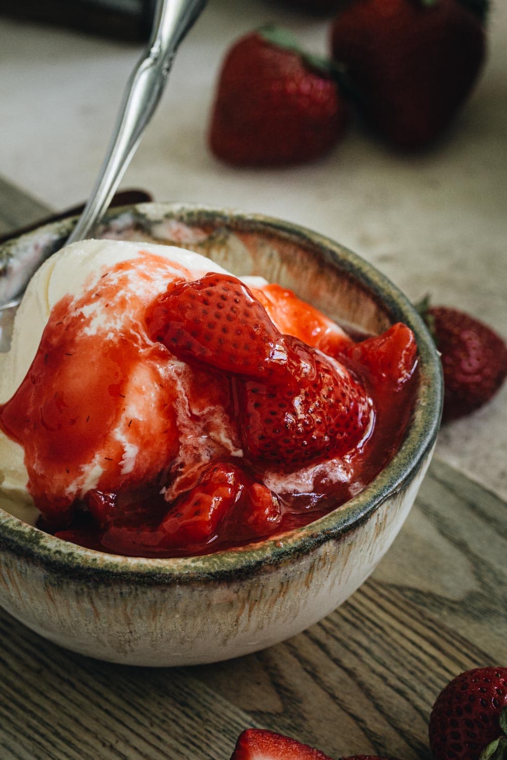 strawberry topping over vanilla ice cream in a pottery bowl with silver spoon