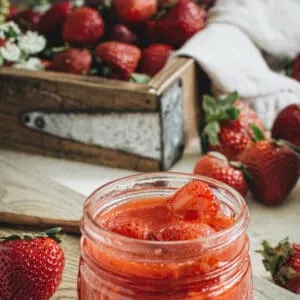 Strawberry sauce in glass jelly jar on wooden cutting board. Image for Pinterest.