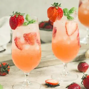 Two strawberry mojitos in tall glasses topped with sliced strawberries and basil leaves.